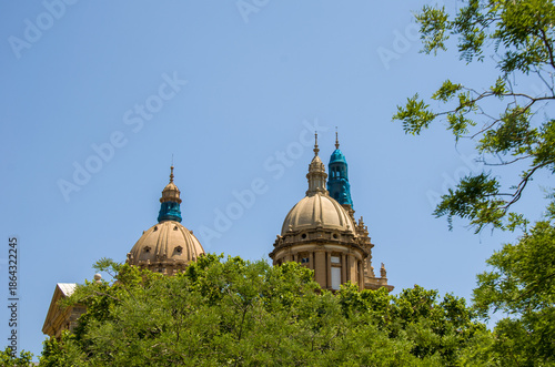 Historic domed building towers behind green trees on clear day