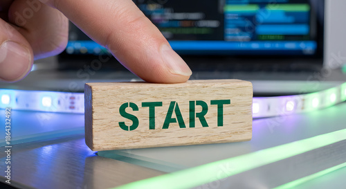 Finger pressing start wooden block, technology startup concept, business launch symbol, coding laptop background, new project beginning, motivation, strategy, web developer office, blurred led lights.