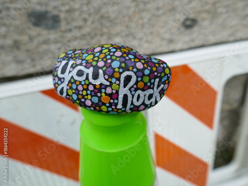 You rock kindness rock on top of green traffic cone at road work site