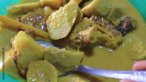 Someone scooping traditional yellow coconut milk taro root curry. Delicious Indonesian authentic cuisine