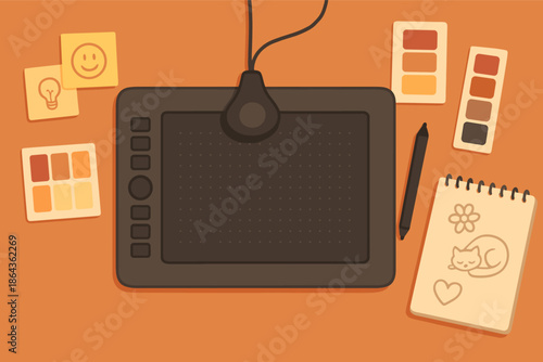 Digital drawing tablet with pen surrounded by swatches and sketchpad on orange desk