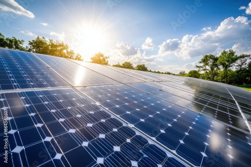 Solar panels collect bright sunlight under a clear blue sky with fluffy clouds.