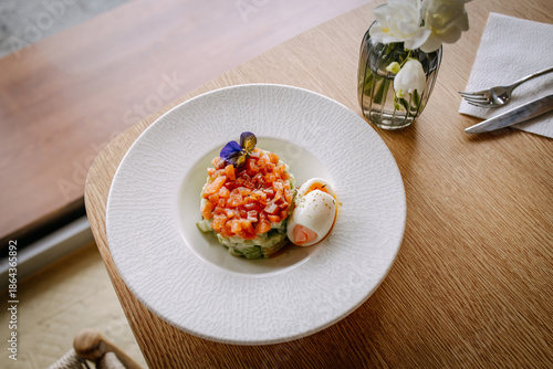 Elegant salmon tartare with soft boiled egg served on a white plate. Minimalist fine dining presentation with natural light, calm tones and refined restaurant atmosphere