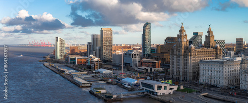 Aerial sunrise view of Liverpool, River Mersey left, skyline right. Royal Liver Building, Cunard Building, Museum of Liverpool, Albert Dock, cranes, wind turbines.