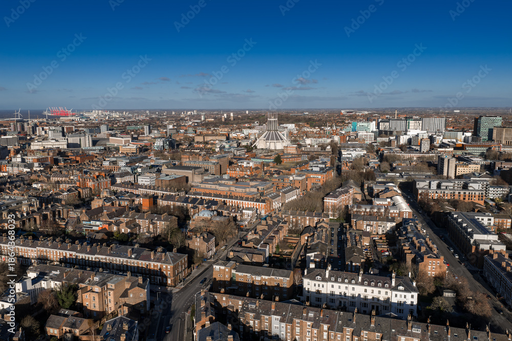 Naklejka premium Aerial sunrise view of central Liverpool, UK. Liverpool Metropolitan Cathedral sits centered. Terraces lead to an urban core, cranes and waterfront sit distant. Crisp winter light casts long shadows.