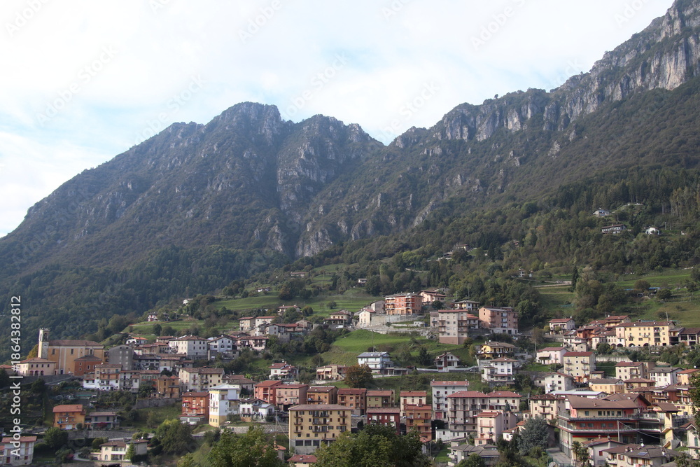 Obraz premium igh-angle panoramic view of the alpine village of Lodrino, situated in the Val Trompia valley, Brescia province. The images capture the traditional Italian mountain architecture, green hillsides