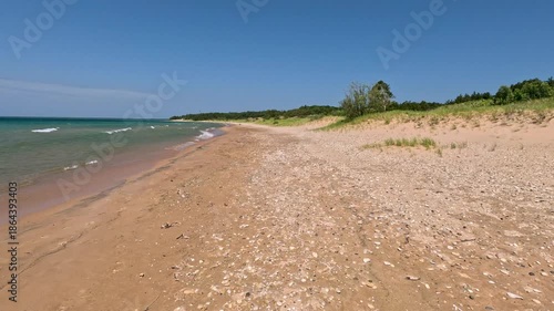 Moving across the the sandy beach of Lake Michigan. Big waves roll onto the shore. Sand dunes and forest line the beach. Unspoiled nature located within Wilderness State Park in Northern Michigan, USA