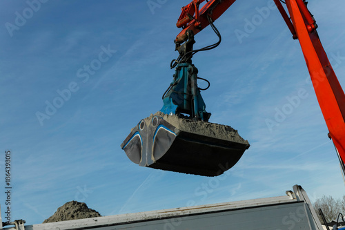Obraz na plátně Hydraulic clamshell grab bucket filled with wet sediment against blue sky