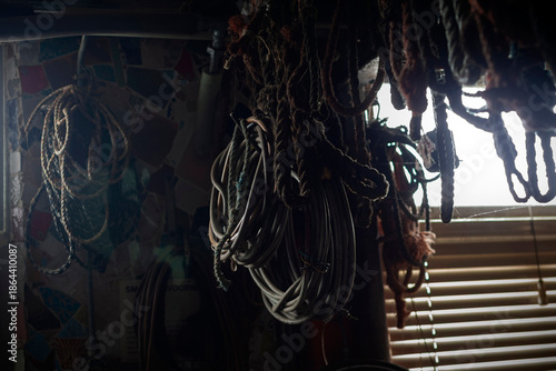 Fotografija Coiled ropes and nautical equipment hanging in maritime workshop with window lig