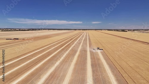 Yellow combine harvester moving through dry wheat paddock and kicking up some dust