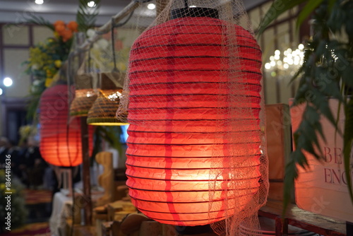 Close-up of elegant white fringe tassels hanging from a lush green ceiling decoration, with sparkling crystal beads and warm golden chandeliers in a soft bokeh background for a wedding event