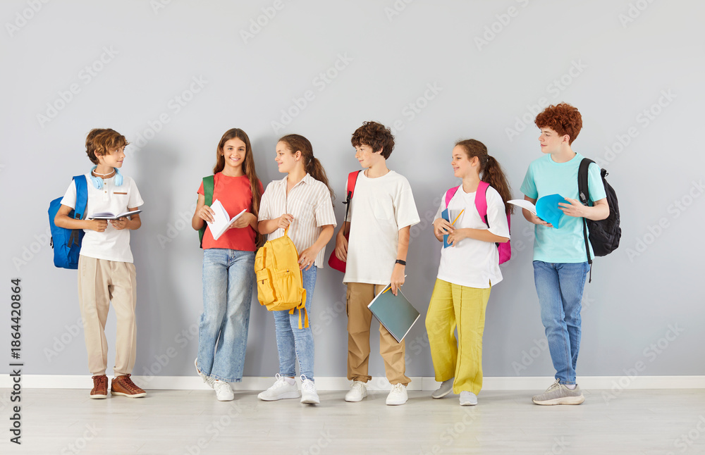 Obraz premium Group of diverse students, including teenagers and children, standing on a grey background, engaged in conversation. They are pupils in a school setting, focused on education and learning.