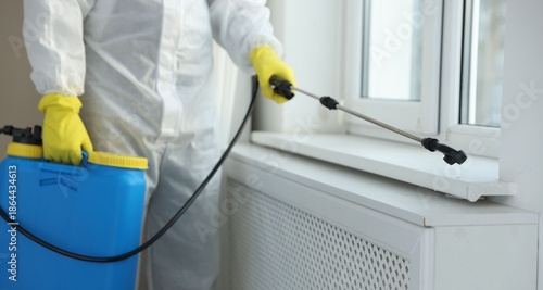 Photography Pest control worker in protective suit spraying insecticide indoors, closeup