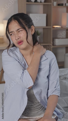 Stressed Asian woman suffering bad neck muscle ache sitting bed feeling unhappy exhausted face hurt from office syndrome health problem tension strain discomfort overworked home bedroom Vertical