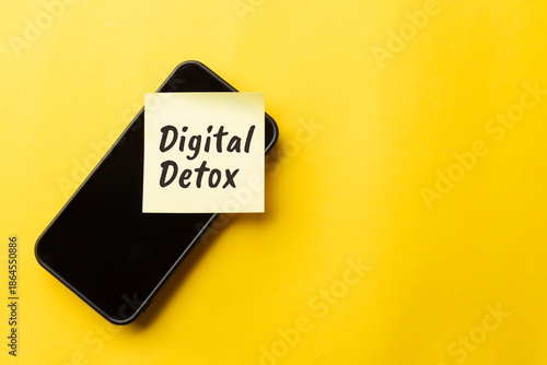 Top view of a hand placing a Digital Detox sticky note on a smartphone. Concept for social media addiction, mental health, tech life balance, and disconnecting from technology for better wellbeing.