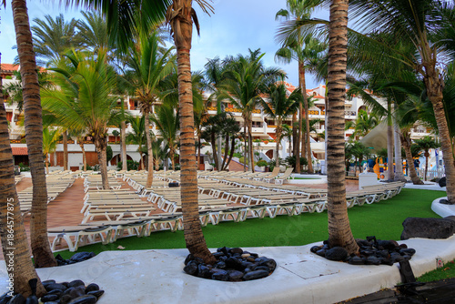 Hotel complex with unoccupied sunloungers and palm trees in the morning in holiday resort Playa de las Americas on Canary Island Tenerife, Spain