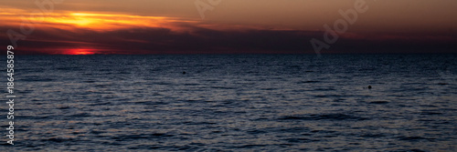 The reflection of the setting sun on the waves. A view of the sea at sunset. The sky over the sea at sunset. In the distance, bright sunbeams and reflections of the warm light of the setting sun glist