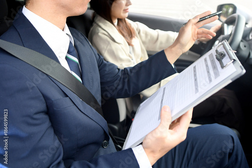 Photos 自動車教習所で指導するアジア人の男性教官と若い女性