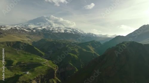 Aerial view of the majestic, snow-capped Mount Elbrus rising under a dramatic sky in the Caucasus Mountains, within Elbrus National Park, Kabardino-Balkaria, Russia.