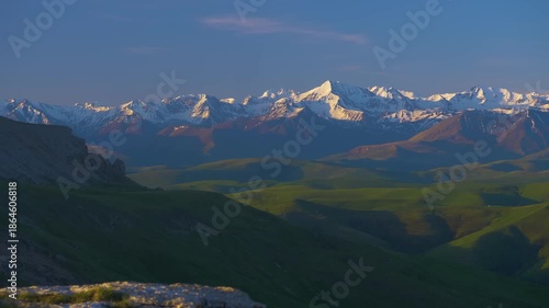 Spectacular panoramic landscape showcasing Mount Elbrus, the highest peak in Europe, surrounded by rugged mountains and lush green valleys on a clear day at sunrise or sunset.