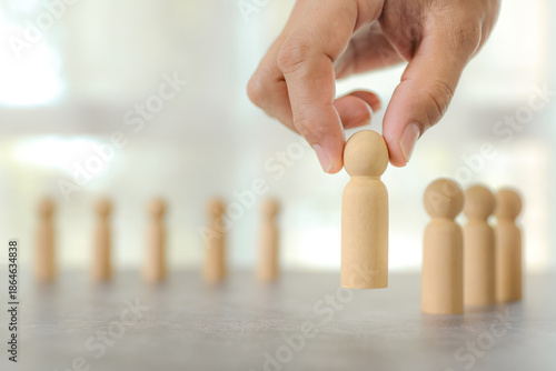 Businessman's hand chooses wooden person stands for HR human resources personal leader training skill or leadership and challenge business team player and organization management teamwork.