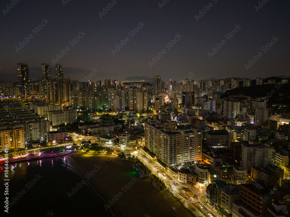 Obraz premium Aerial drone view of Busan city skyline at night with illuminated buildings and coastal waterfront, South Korea