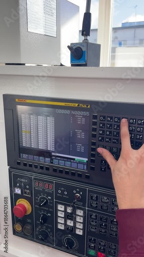 CNC machine operator enters program data into the machine's computer using the control panel keyboard, setting up parameters for precise workpiece machining.