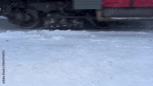 Close-up view of train wheels rolling through snow in winter, kicking up powder and leaving deep tracks on the icy rails during cold weather travel.