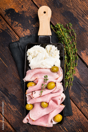 Italian antipasto with Sliced Prosciutto Cotto ham, green olives and mozzarella. wooden background. top view