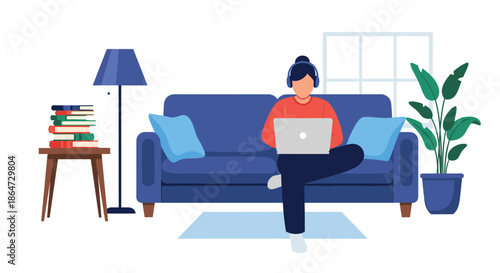 Young person sitting comfortably on a blue sofa while working on a laptop with headphones on in a cozy home environment.