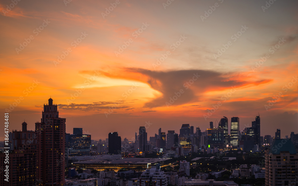 Fototapeta premium Dramatic sunset over modern city skyline - Golden sunset light illuminating a modern city skyline with dramatic clouds and evening atmosphere 