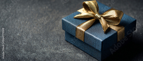 Dark Blue Textured Gift Box with a Golden Satin Ribbon and Bow on Dark Grey Slate Background