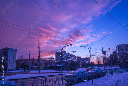 Winter evening in a residential area: silhouettes of panel buildings and bare trees against a pink and blue sunset.