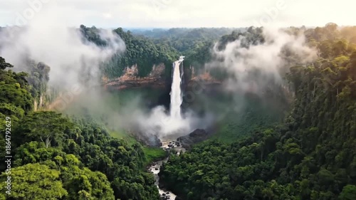 Cinematic aerial view of a majestic waterfall in a lush tropical jungle with mist and a rainbow at sunset