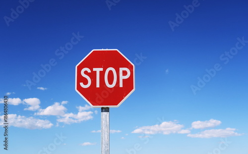 Stop. Inscription STOP en blanc  sur un panneau octogonal rouge bordé de blanc. Fond de ciel bleu.  Panneau de signalisation routière.