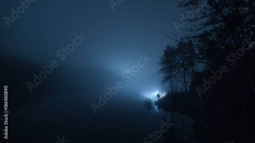 Schilderij op canvas Silhouette of a lone person with flashlight standing by foggy lake at night