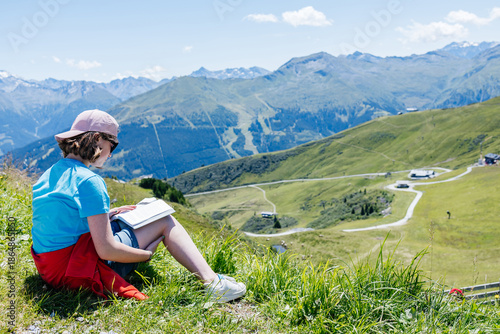 Young girl reading a book enjoying the mountain view in summer