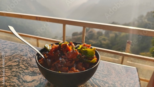 Mushrooms Manchurian dry in black bowl with beautiful view of mountains. Mushroom Manchurian - is indo chinese cuisine dish with deep fried mushrooms, bell peppers, sauce, capsicum and onion.