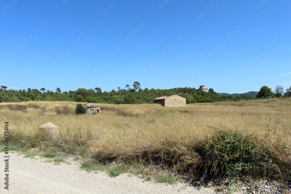 Fototapeta premium Empty field with rural houses along the route from Montserrat to Manresa in Catalonia, Spain, taken in July 2024.