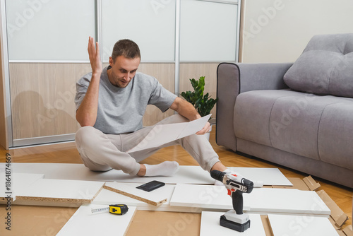 A confused man gesturing while reading furniture instructions among scattered parts and tools in a bright modern room DIY troubleshooting content hardware store advertising home renovation blogs