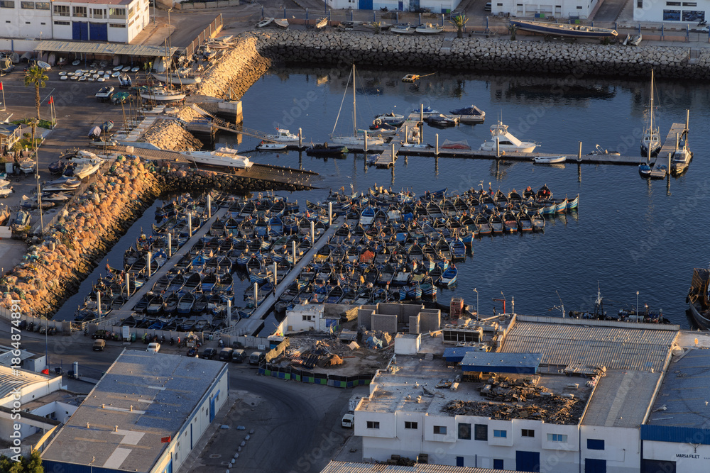 Fototapeta premium Harbor Marina With Rowboats Docked Along Breakwater Under Industrial Waterfront, Agadir, Morocco