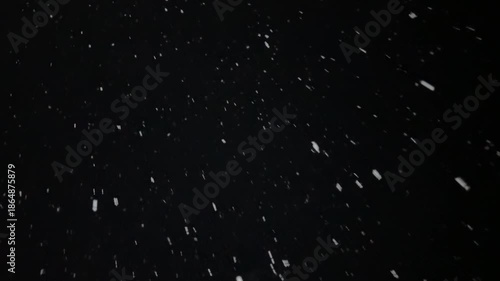 thick snow falls at night in the light of a streetlamp, snowflakes swirl in the wind and rush away against a black background.