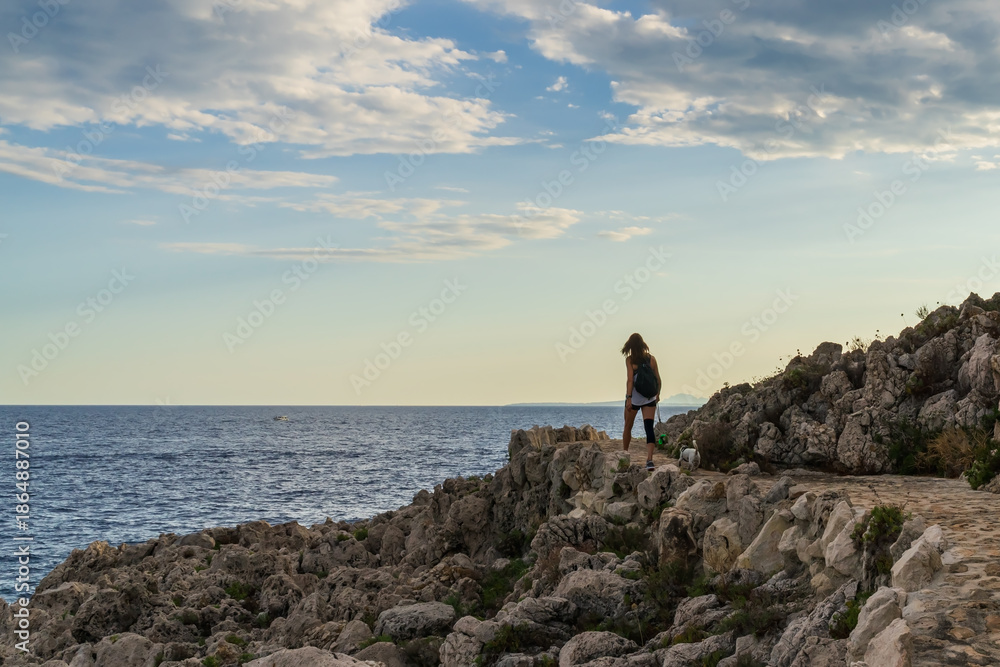 Obraz premium Young woman hiking with her dog along the rocky coastal path of Saint-Jean-Cap-Ferrat overlooking the Mediterranean Sea in France.