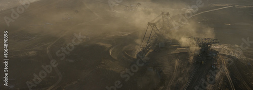 High resolution panoramic view of massive mining machines in an open pit coal mine, surrounded by dust. Powerful industrial scene showing large scale extraction, energy production, and human impact.