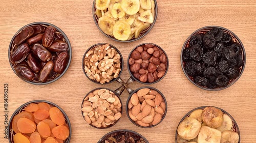 Dried fruits and different types of nuts in decorative glass bowls on the wooden table. Top view. Tilt down shot. Healthy eating concept.