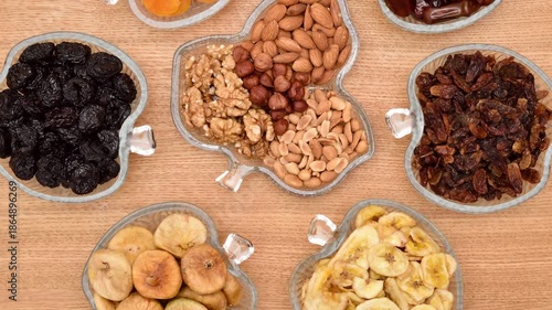 Dried fruits in apple-shaped glass bowls and different types of nuts in leaf-shaped glass bowls on the wooden table. Top view. Healthy eating concept.