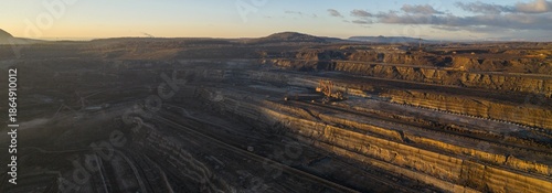 High resolution panoramic view of an open pit coal mine with mining machines, layered terrain. Industrial landscape showing large scale extraction, energy production, and environmental impact. © Jag_cz