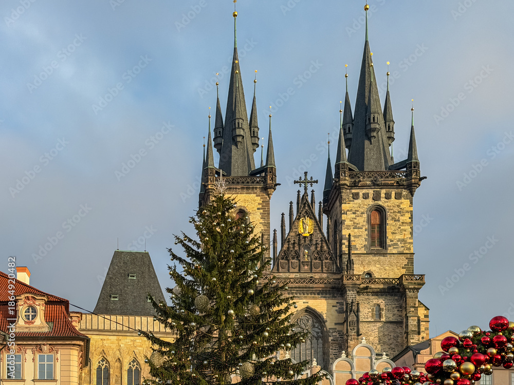 Fototapeta premium The Gothic twin spires of the Church of Our Lady before Týn rise majestically behind a decorated Christmas tree in the Old Town Square of Prague, Czechia, capturing the festive spirit of winter.