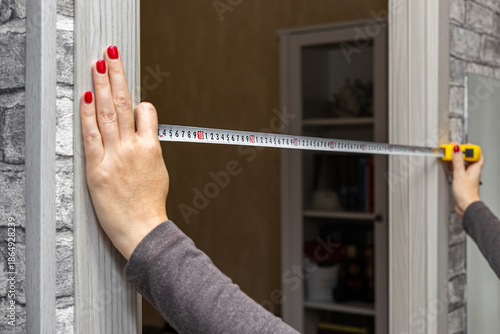 A woman measures a doorway with a tape measure. a measuring tape in a woman's hands. woman doing home renovations. independent woman