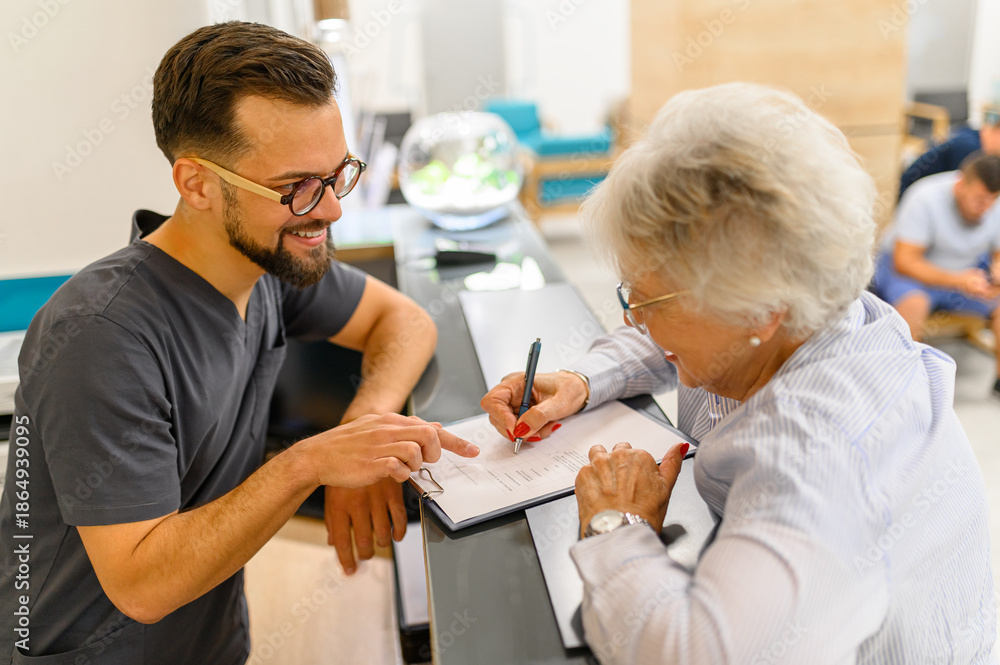 Obraz premium High angle view of male receptionist guiding senior patient while filling medical document at hospital desk